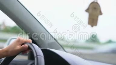 司机在仪表板和挡风玻璃背景下的方向盘上的手